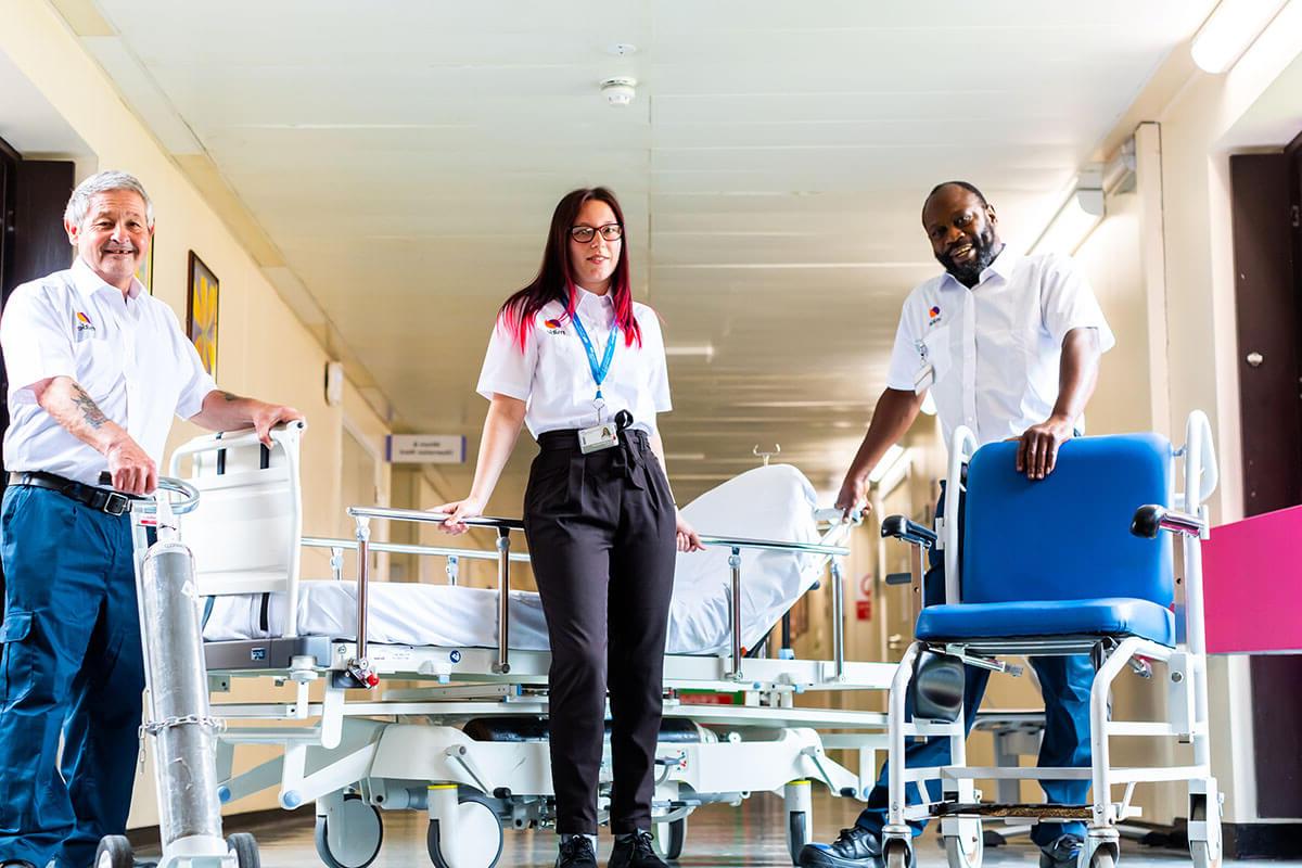 Three Mitie workers standing in a hospital corridor with various healthcare equipment